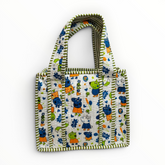 Front view of a white quilted cotton kids lunch bag featuring colorful cartoon pig character prints and olive green and white striped handles.