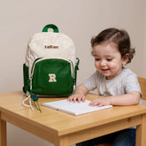Tiny Tokens cream and forest green two-tone polyester kids backpack with varsity R patch and bear charm.