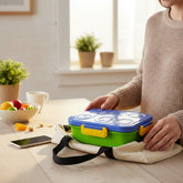 Tiny Tokens blue and green lunch box with embossed shapes on lid and yellow clasps. Includes steel inner tray, sauce cup, spoon, and fork.