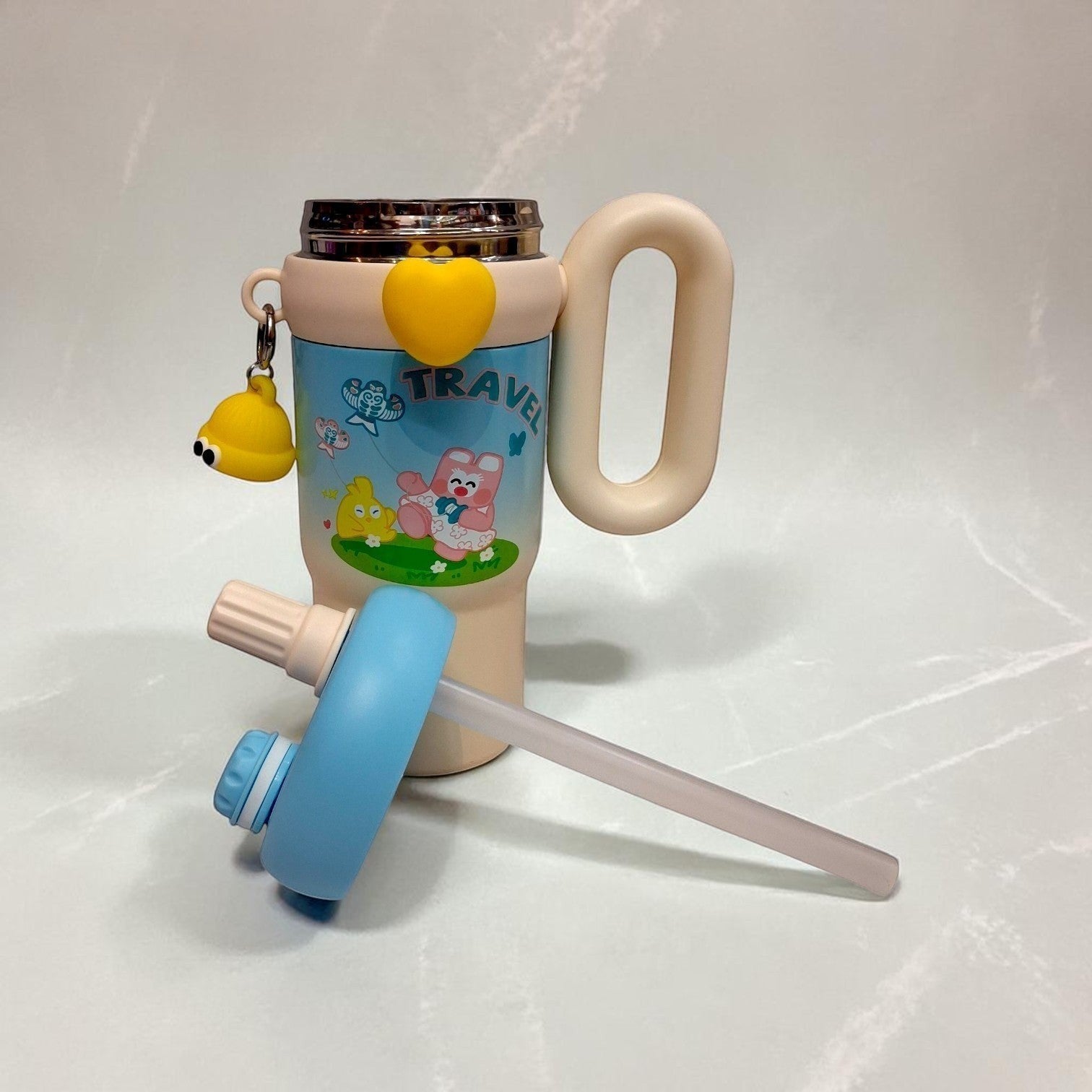Tiny Tokens pastel blue and cream kids travel tumbler with handle and straw, featuring cartoon animals and a yellow heart charm.