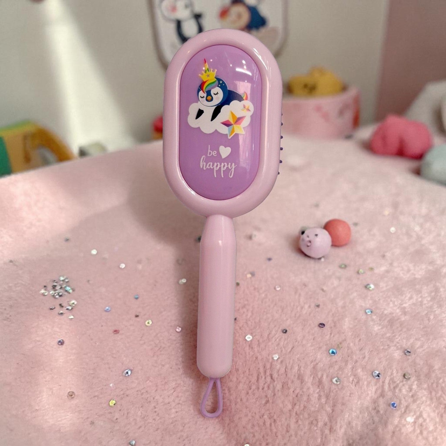 Tiny Tokens pink and purple cartoon hair brush with a penguin design and 'be happy' text, featuring soft bristles and a cushion base for detangling.