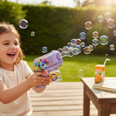 A happy young girl plays with a purple automatic bubble gun featuring a cartoon unicorn. Bubbles stream from the gun in a sunny outdoor setting.
