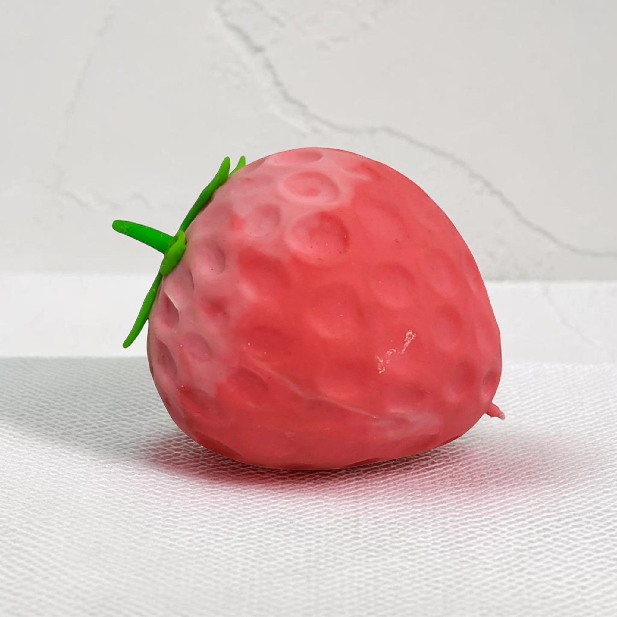 Tiny Tokens red strawberry stress relief toy with green stem, made of soft rubber with dimpled texture.
