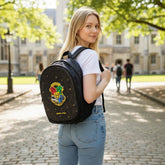 Tiny Tokens Harry Potter Hogwarts backpack in black with the Hogwarts crest and gold accents. A young woman wears it outdoors.