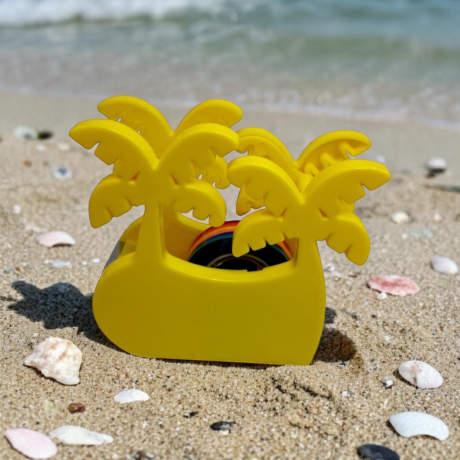 Tiny Tokens yellow palm tree shaped tape dispenser with rainbow tape roll for kids' desks.