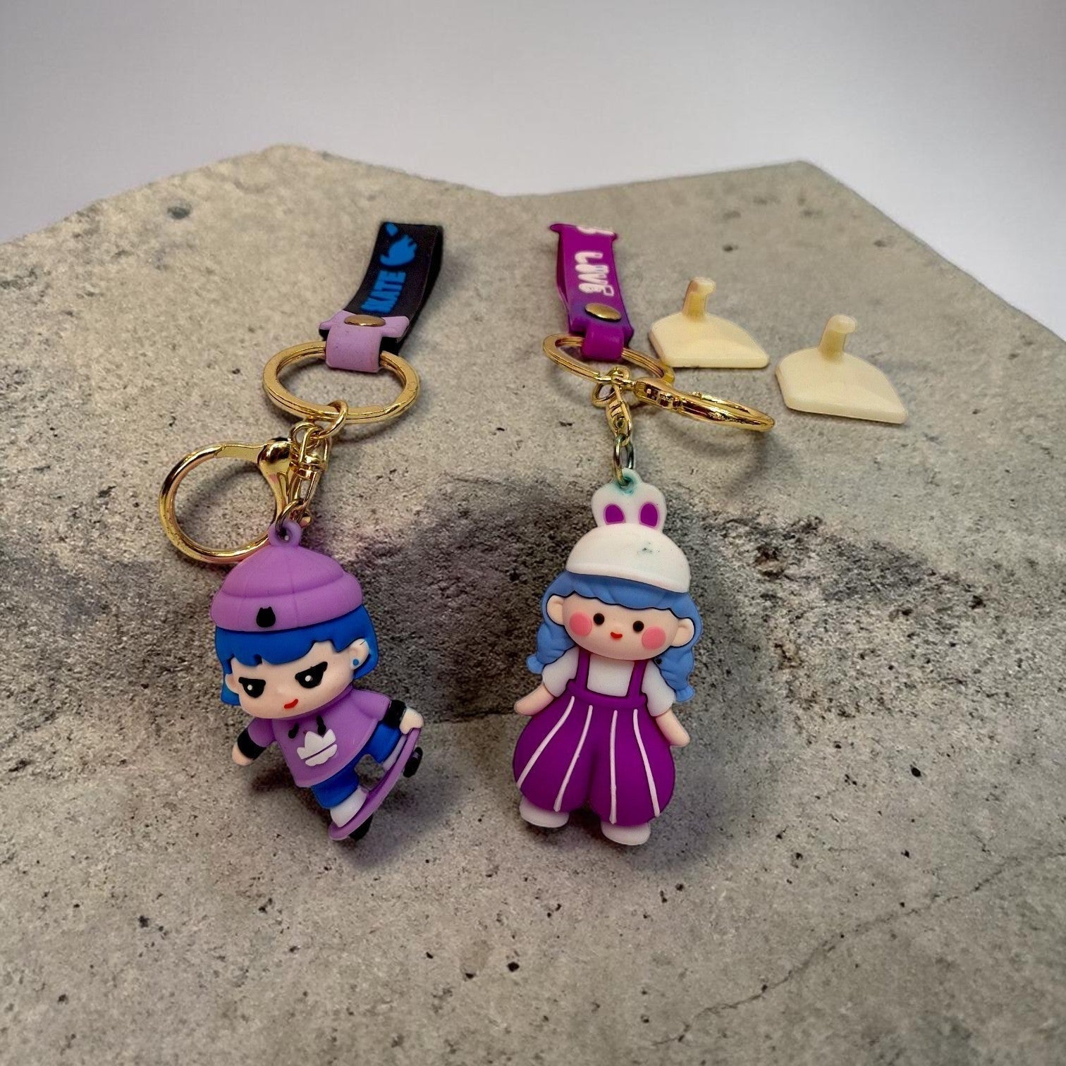 Tiny Tokens cartoon 3D rubber keychains featuring a skater girl in purple and a princess doll in purple with gold hardware.