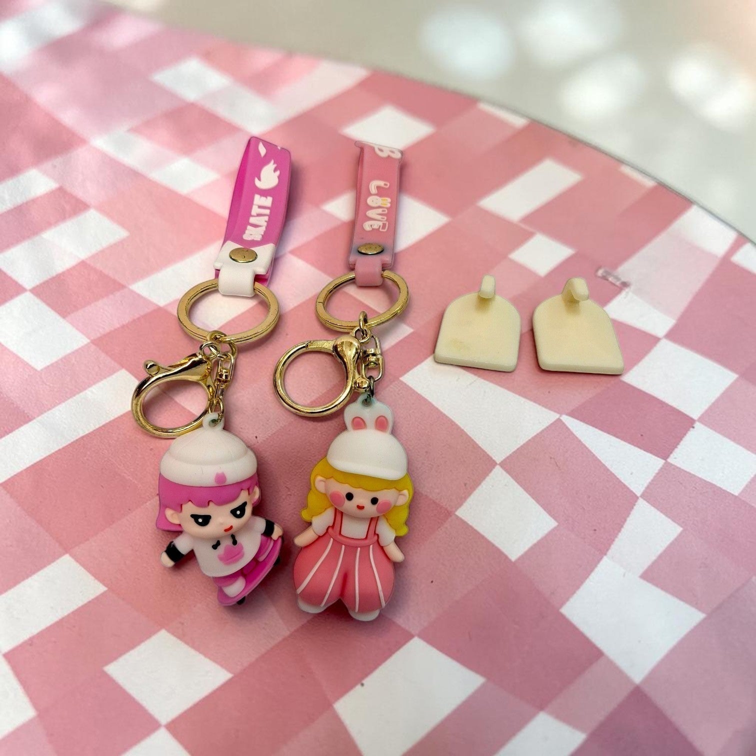 Tiny Tokens pink and white cartoon character rubber keychains with gold hardware and themed straps, one skater girl, one princess doll.