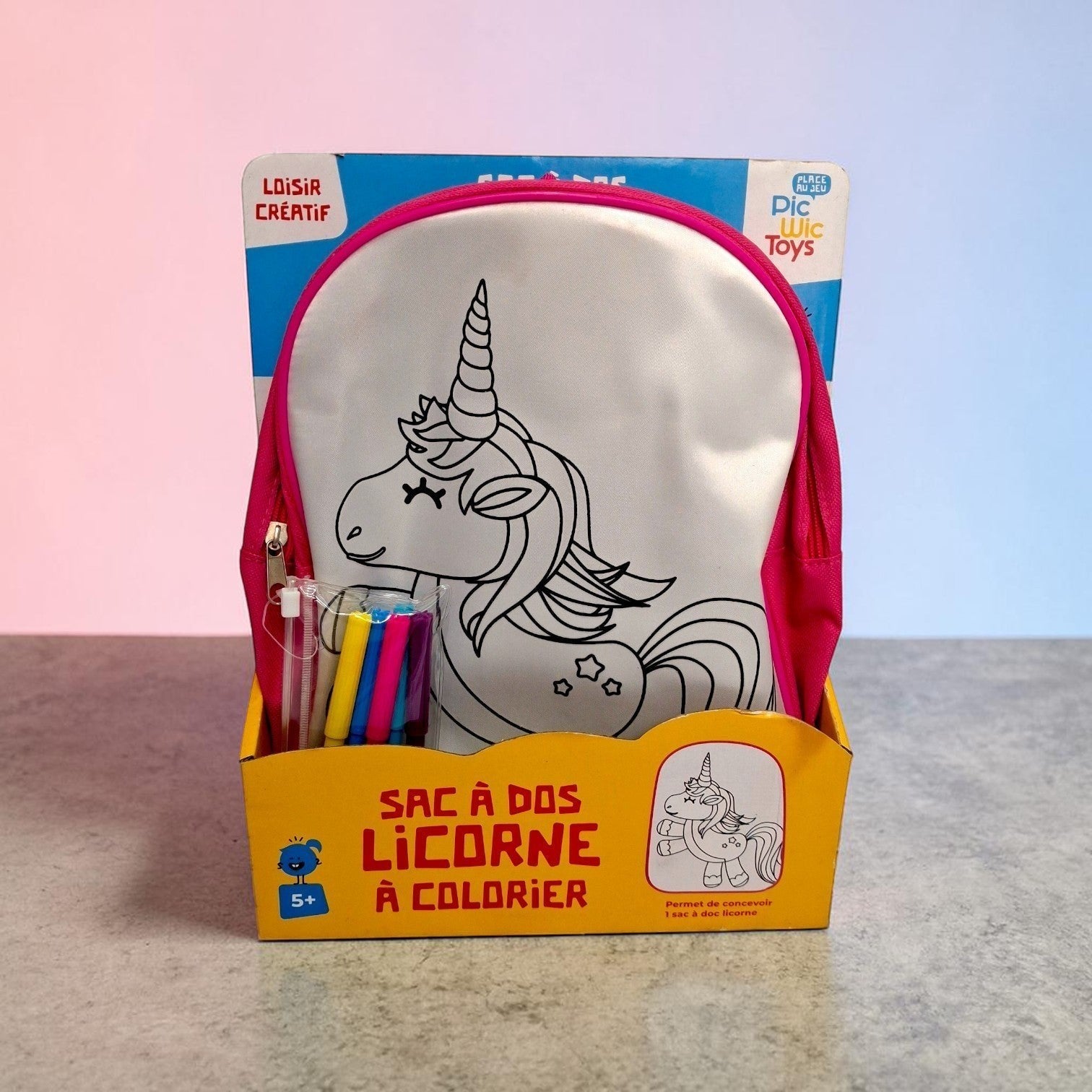Tiny Tokens kids' DIY unicorn backpack with pink trim, ready to be coloured with included fabric markers. Features a white canvas front panel with a black unicorn outline.