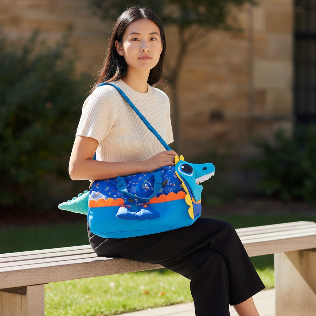 Tiny Tokens blue polyester duffle bag with space print, 3D dinosaur face, yellow spikes, and rocket pockets.