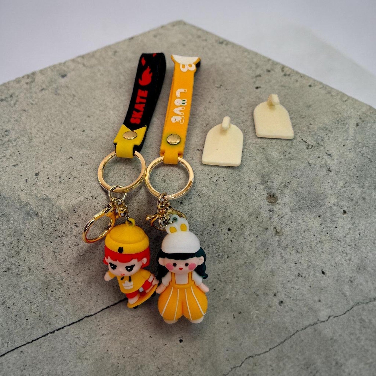 Tiny Tokens yellow and black rubber keychains with cartoon figures and gold hardware. One has a 'SKATE' strap, the other a 'LOVE' strap.
