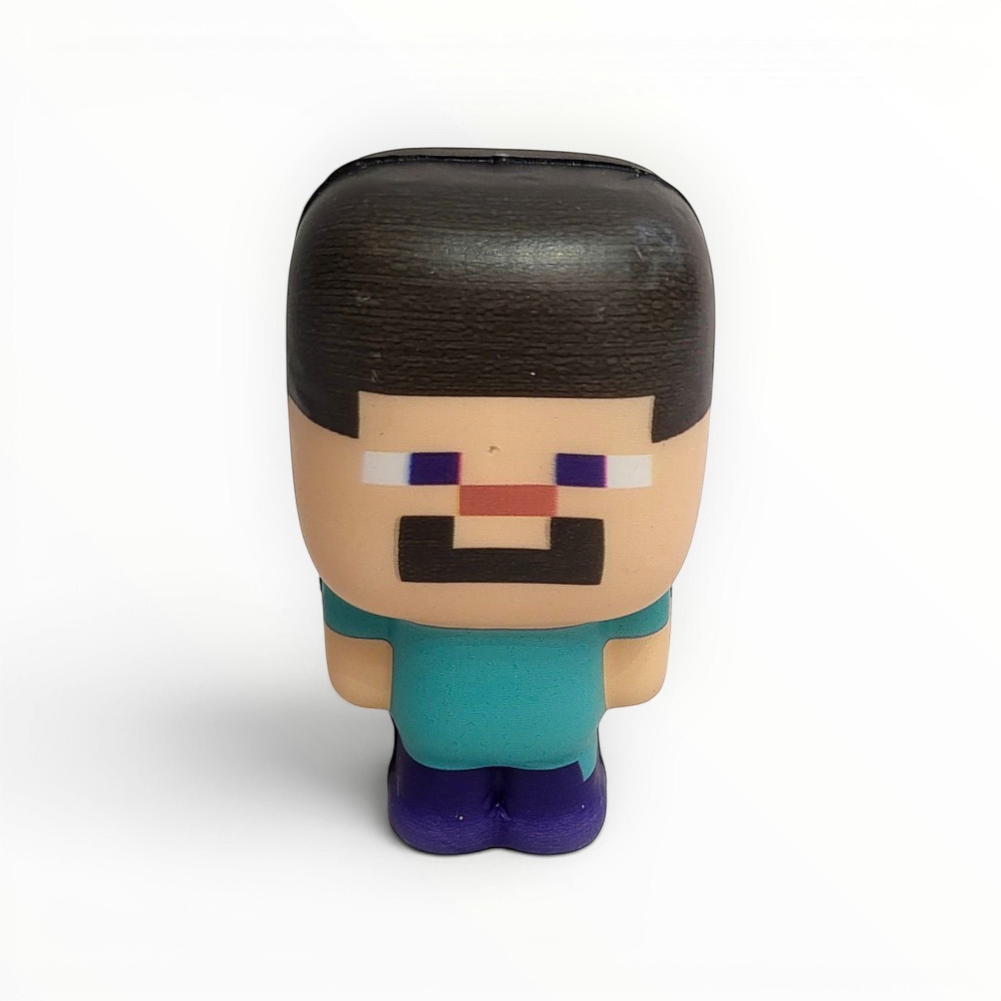 Tiny Tokens Minecraft Steve pixel character squeeze toy, teal shirt, purple pants, soft rubber, for stress relief and play.