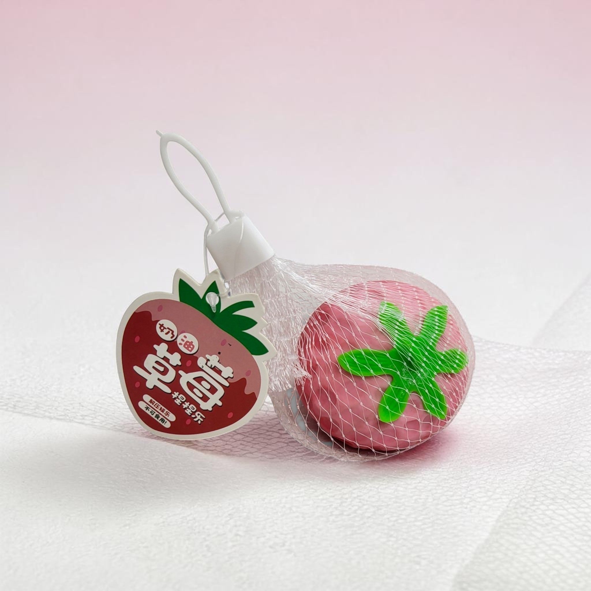 Tiny Tokens strawberry squeeze stress relief toy for kids, pink squishy sensory ball with green stem, made of soft rubber.