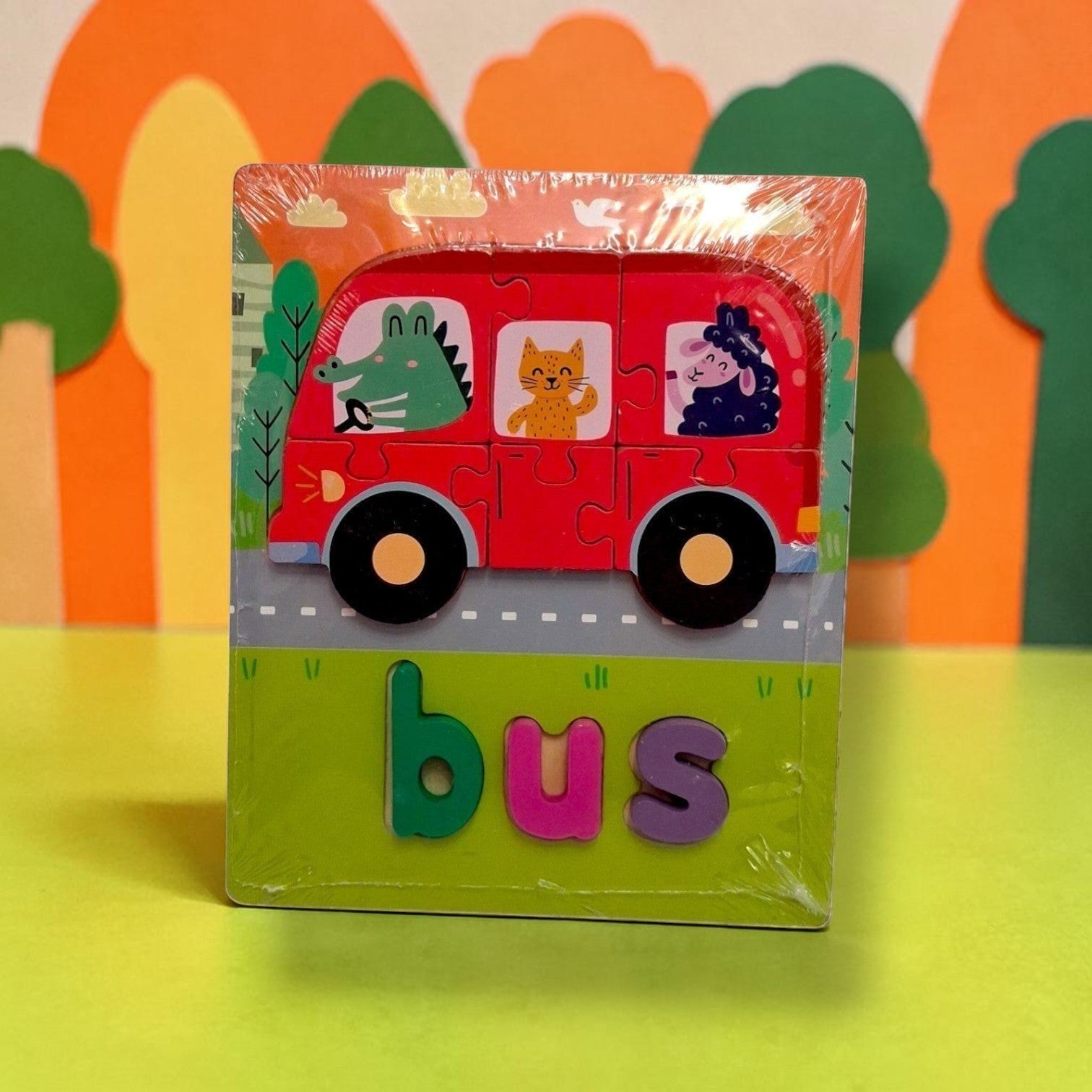 Tiny Tokens wooden bus puzzle with 3D letters for learning to spell 'bus'. Features a red bus with animal passengers and a colourful background.