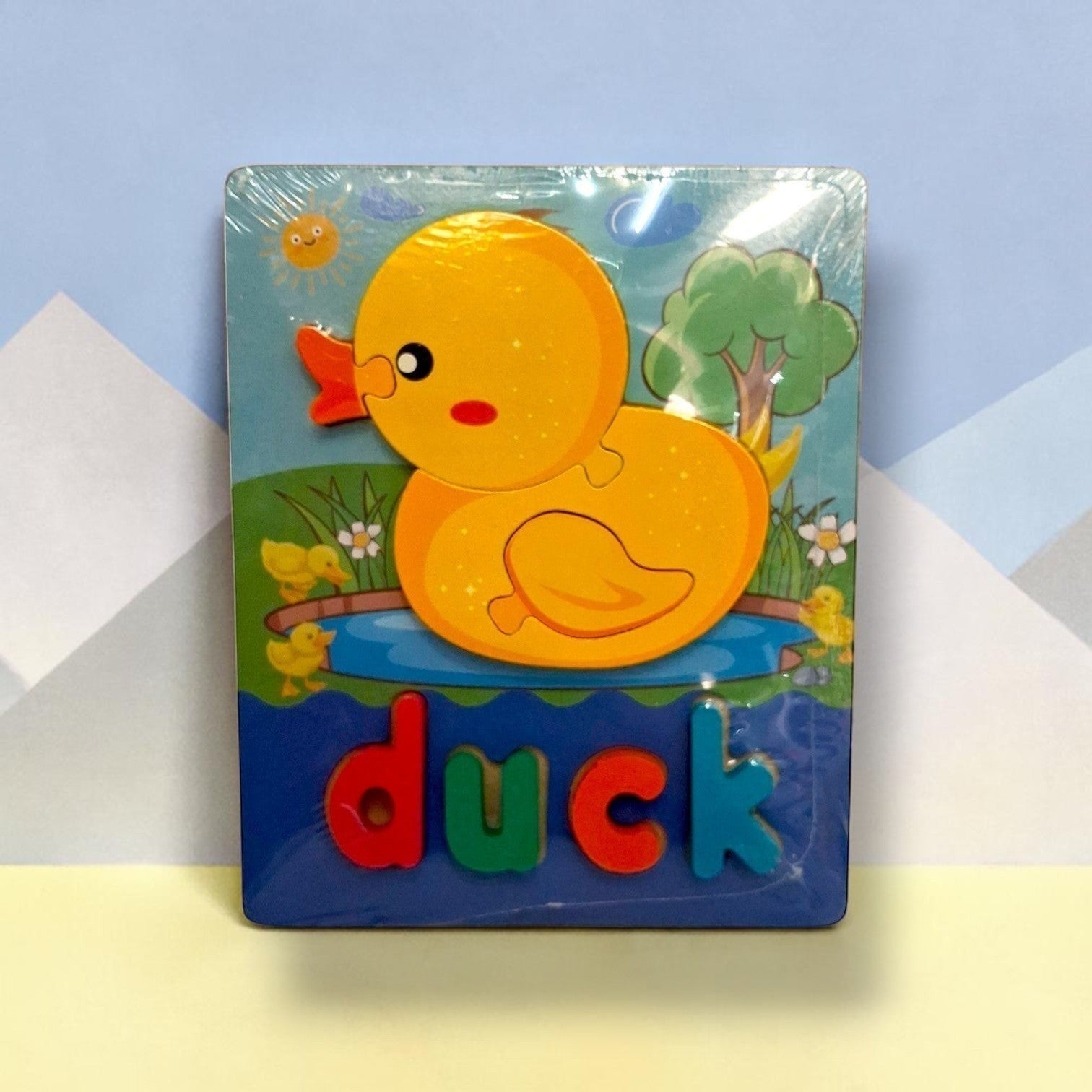 Tiny Tokens wooden duck puzzle board with chunky 3D letters spelling 'duck'. Features a yellow duck and ducklings in a pond with a tree and sun.